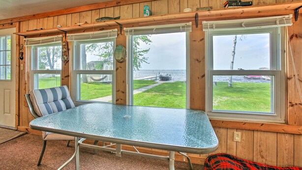 Ein Zimmer mit Tisch mit Glastischplatte und einem gestreiften Stuhl, große Fenster mit Blick auf eine Grünfläche und ein Gewässer, sowie Holzvertäfelung an den Wänden.