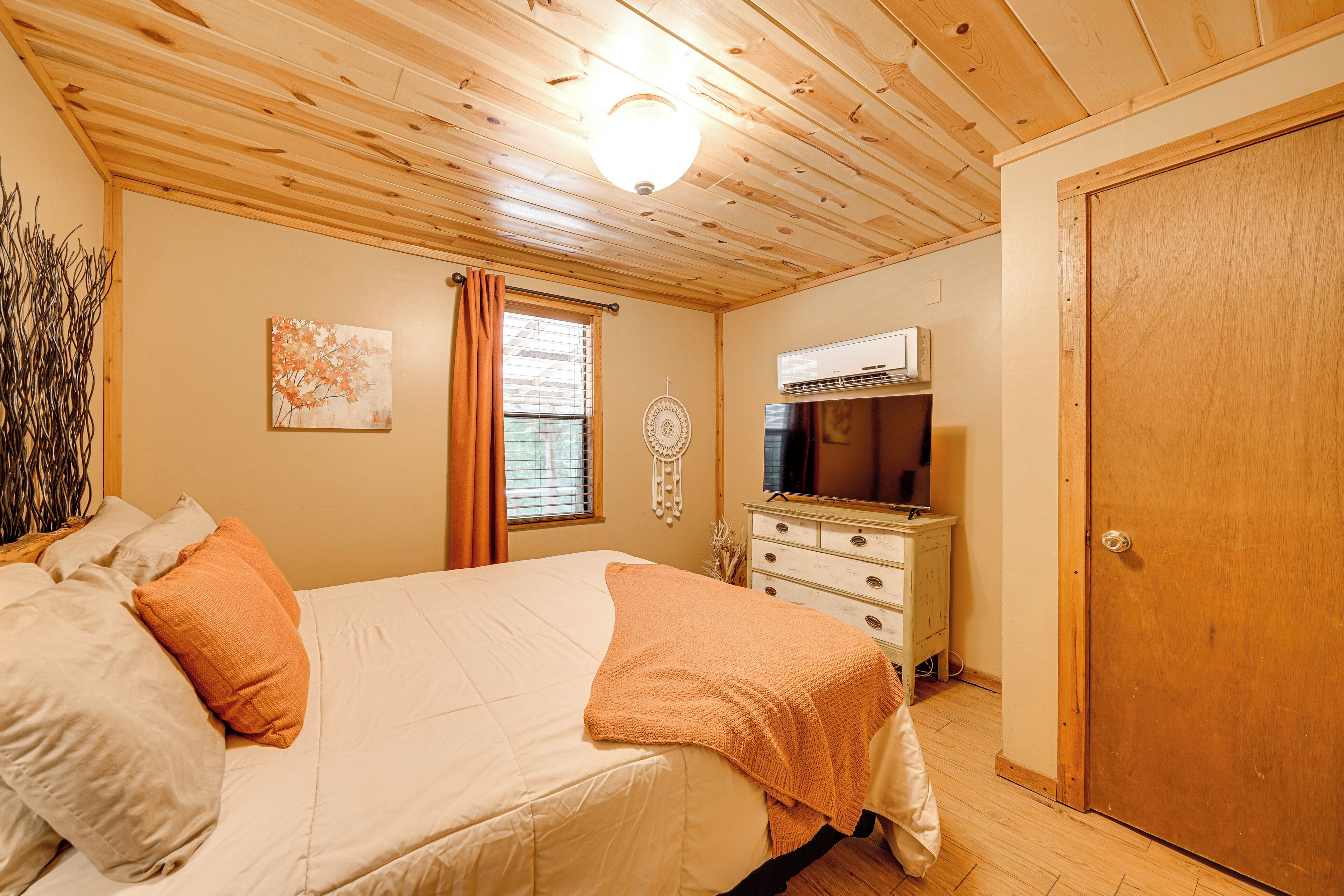Un dormitorio con cama, cómoda, armario, ventana con cortinas y aire acondicionado instalado en la pared.