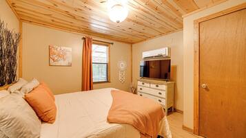 Un dormitorio con cama, cómoda, armario, ventana con cortinas y aire acondicionado instalado en la pared.