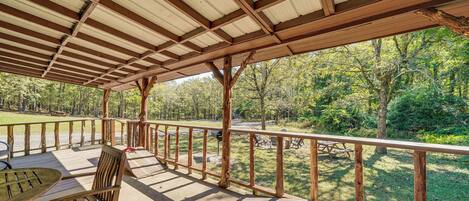 Un espacio al aire libre cubierto con un banco de madera, una mesa y vistas a un área boscosa.