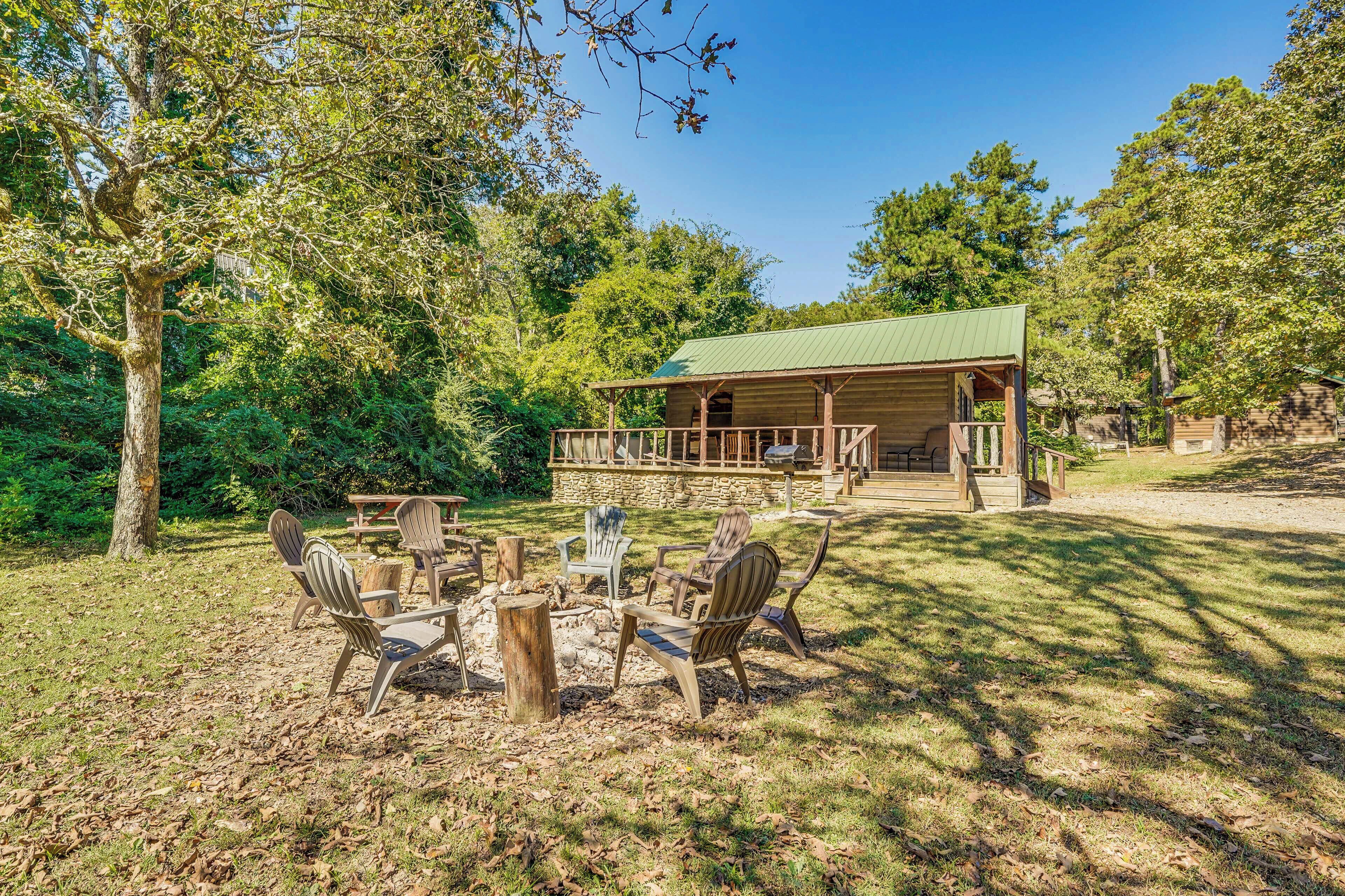 A wooden cabin with a porch, surrounded by trees and a picnic table with chairs.