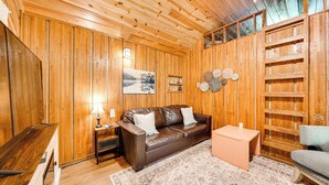 A wooden-paneled room with a brown leather sofa, a small table, and a chair. - Rustic Cabin w/ Hot Tub Near Broken Bow Lake! (Broken Bow)
