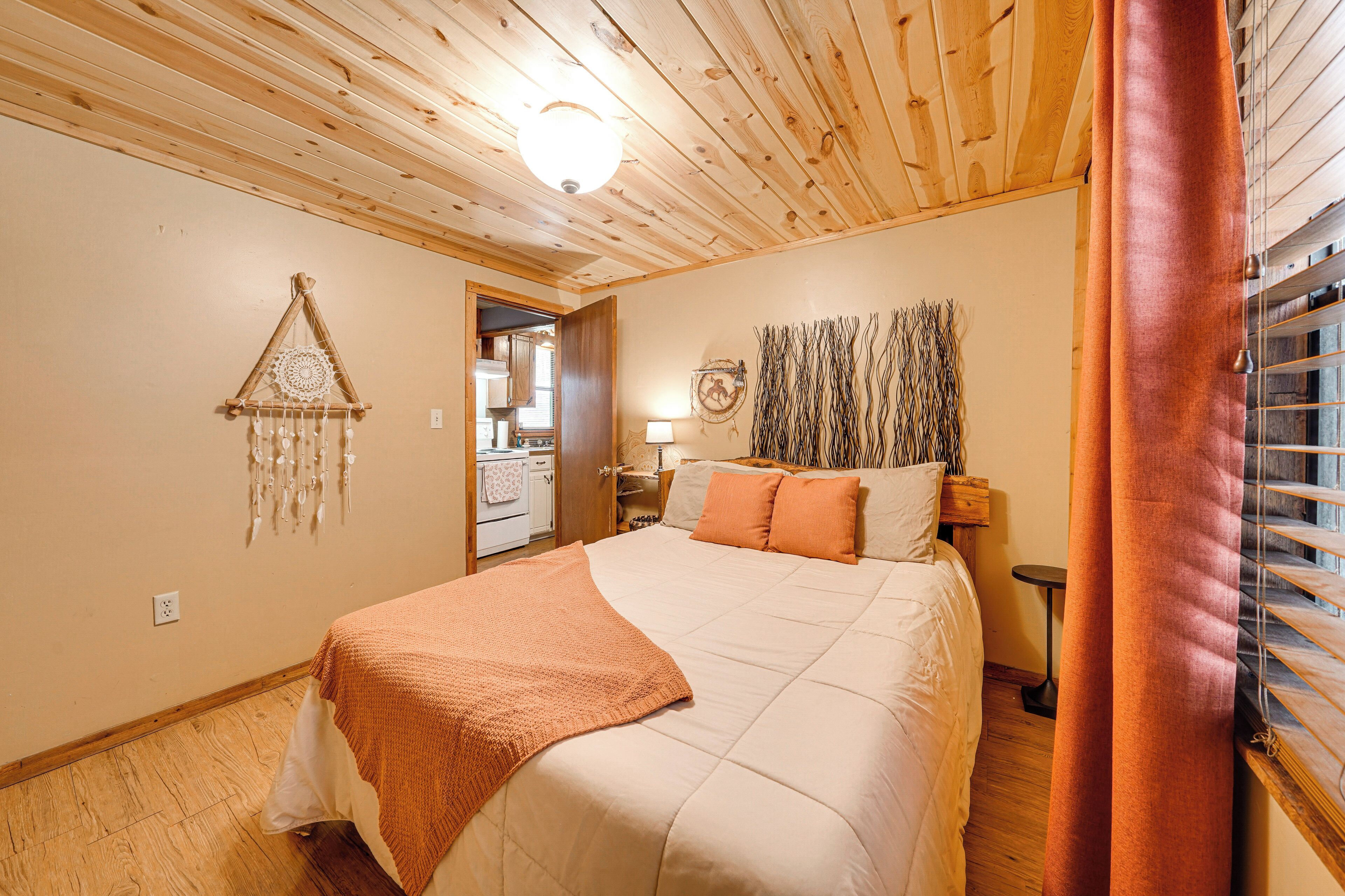 Un dormitorio con techo de madera, una cama con manta blanca y naranja, un tapiz en la pared y una ventana con persianas.