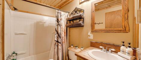 Un baño con techo de madera, bañera, inodoro, lavamanos con dispensadores de jabón y un espejo.