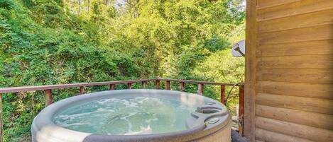 A hot tub on a wooden deck with a view of dense green trees.
