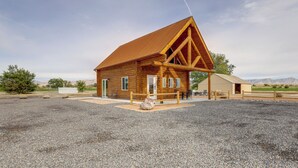 A wooden log cabin with a triangular roof, a gravel driveway, and a fenced area with outdoor seating. - Secluded Grand Junction Getaway w/ Sweeping Views! (Grand Junction)