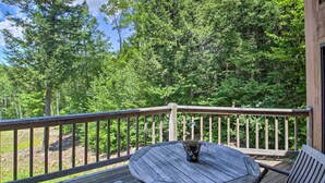 A wooden deck with a round table and chairs, surrounded by a wooden railing, overlooking a forested area. - Bartlett Condo w/ Mtn-view Deck < 1 Mi to Skiing! (Bartlett)