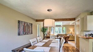 A spacious dining area with a long wooden table, white chairs, and a hanging light fixture. - Bartlett Condo w/ Mtn-view Deck < 1 Mi to Skiing! (Bartlett)