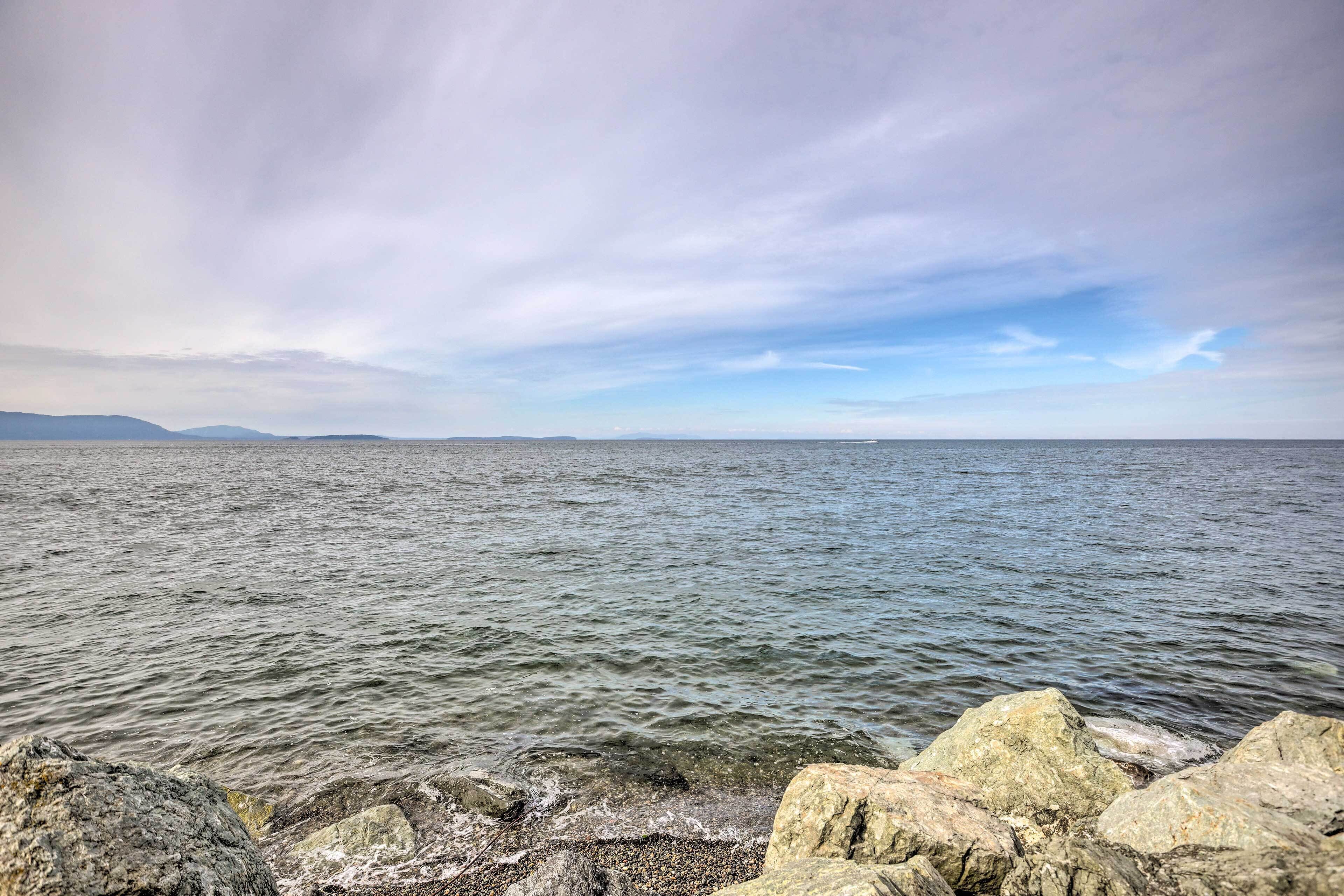 Una costa rocosa con aguas tranquilas y montañas lejanas bajo un cielo nublado.