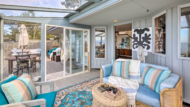 A cozy living area with a sofa, a wicker side table, and a glass door leading to a deck. - Oceanfront Ferndale Oasis w/ Fire Pit, Grill! (Ferndale)