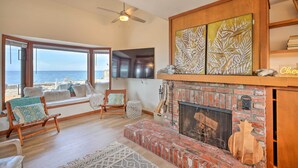 A living room with a fireplace, large windows overlooking the beach, and a ceiling fan. - Oceanfront Ferndale Oasis w/ Fire Pit, Grill! (Ferndale)