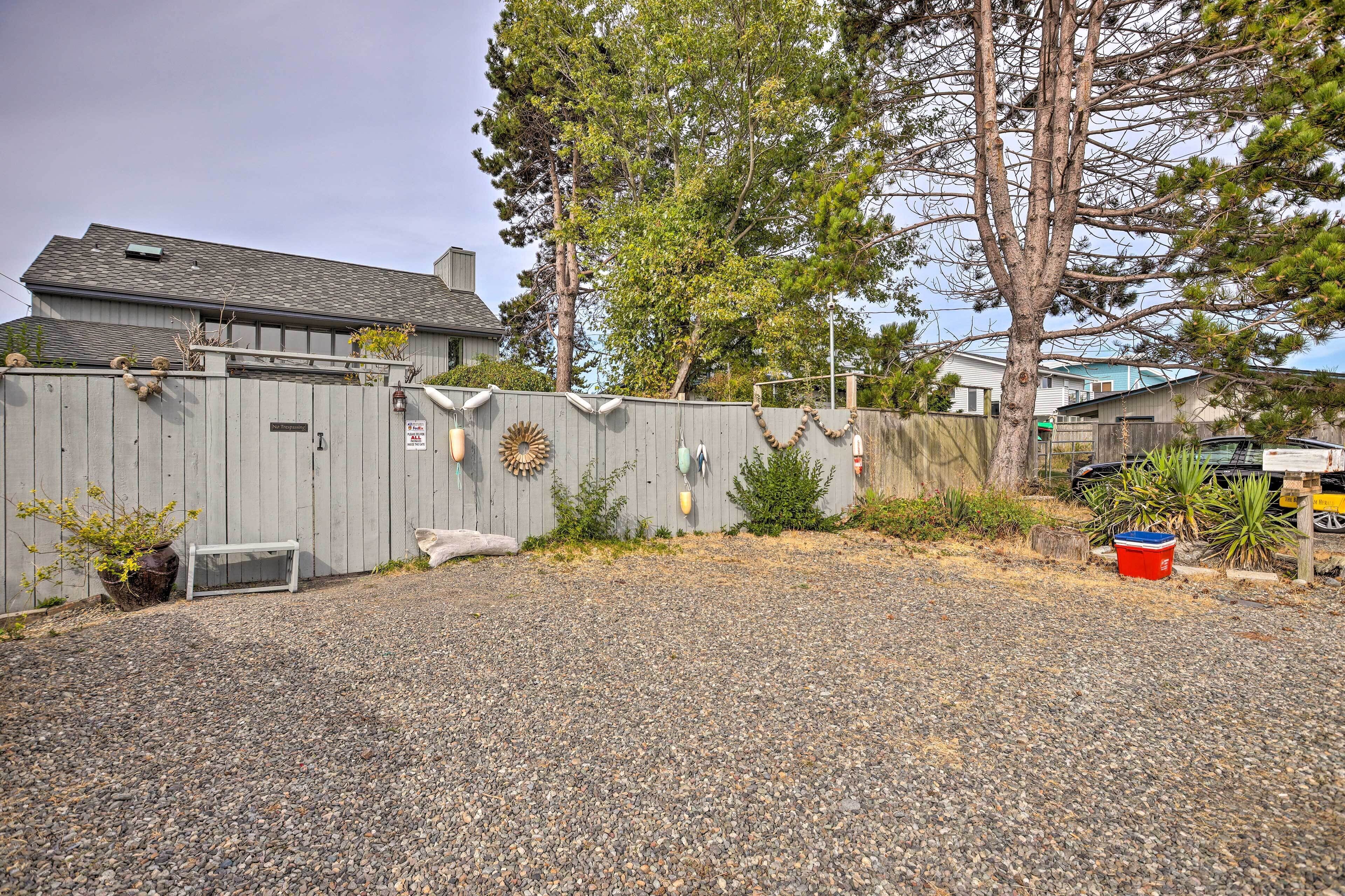 A residential backyard with a gravel driveway, a wooden fence, and a house in the background.