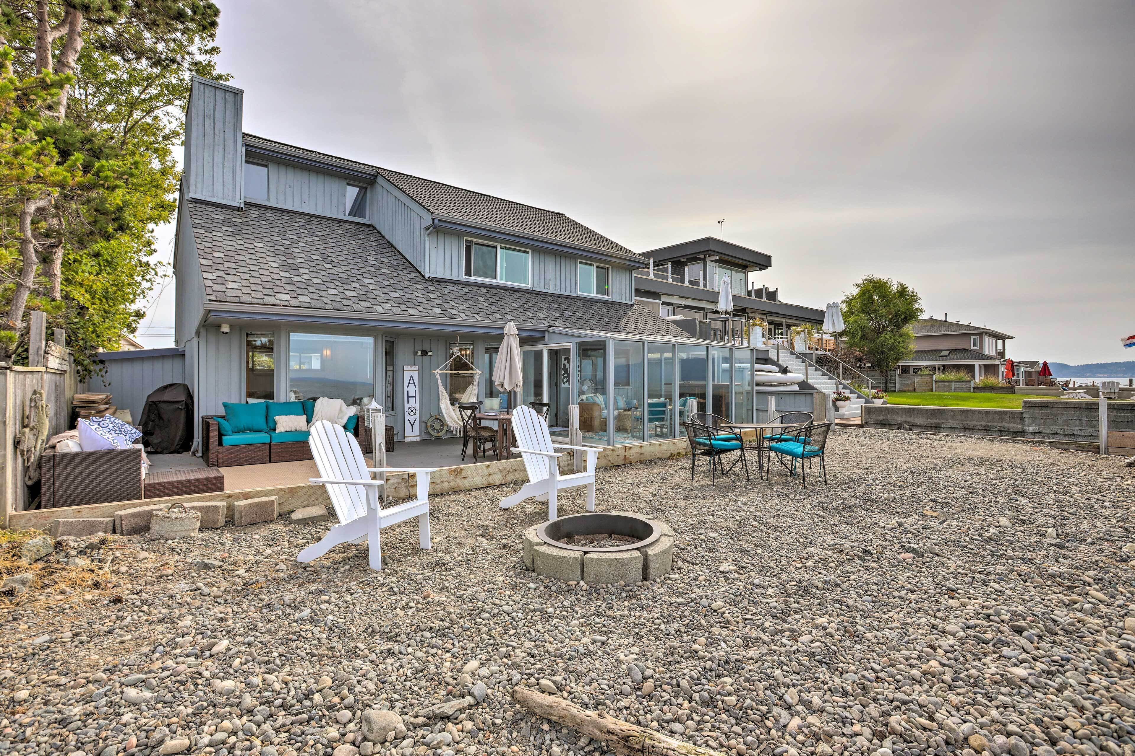 A modern house with a glass-enclosed patio, outdoor seating, and a fire pit.