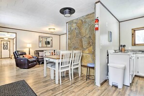A modern living room with a dining area, stone accent wall, and a kitchen with a washing machine. - Creekside Cabin < 2 Mi to Hike, Bike & Ski! (Palmer)