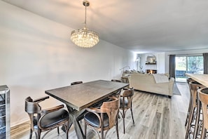 Uma sala de jantar moderna com uma mesa e cadeiras de madeira, um candelabro e vista para a sala de estar.