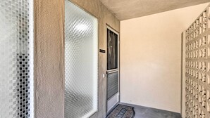 Ein Flur mit strukturierter Wand, einer Tür mit satiniertem Glasfenster und einem Metallgitter auf dem Boden.