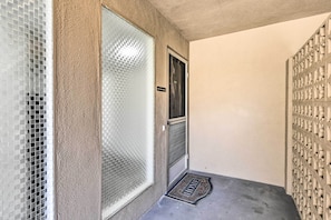 Um corredor com parede texturizada, porta com painel de vidro jateado e grelha metálica no chão.