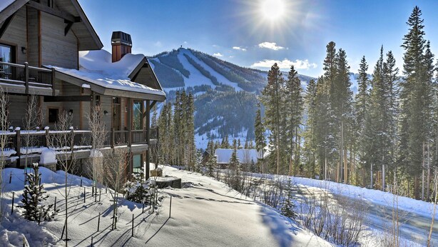 A large lodge with a ski slope in the background, wooden exterior, and a balcony.