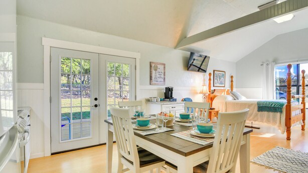 A dining area with a wooden table set for four, white chairs, and a view of the backyard through glass doors. - Ranch Cabin w/ Decks, 10 Mi to Fredericksburg (Fredericksburg)