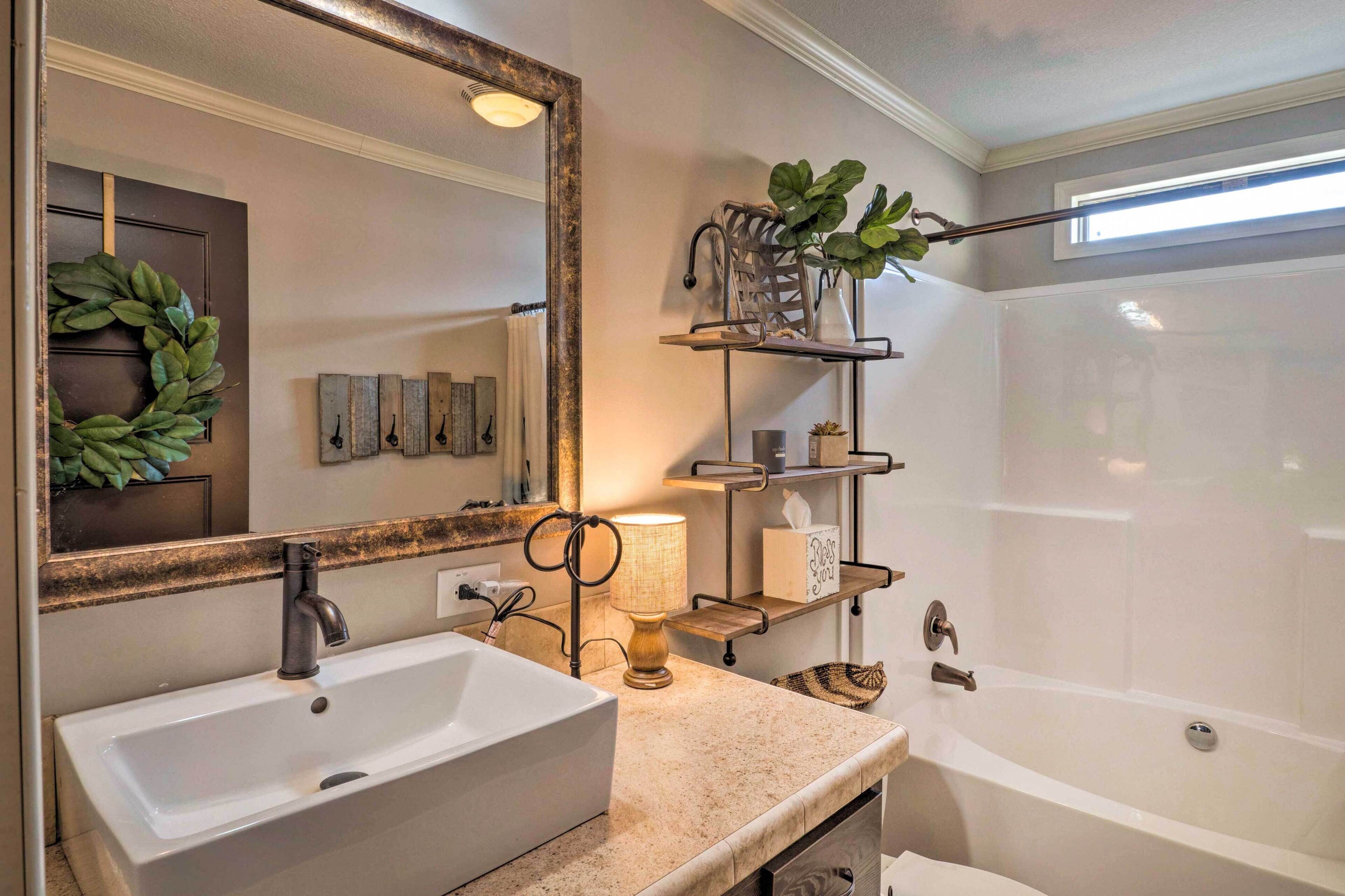 Une salle de bain avec un grand miroir, un lavabo, une baignoire et une étagère sur laquelle est posée une plante.