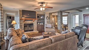 A spacious living room with a fireplace, leather sofas, a flat-screen TV, and a ceiling fan. - Waterfront Louisiana Vacation Rental w/ Dock! (Many)