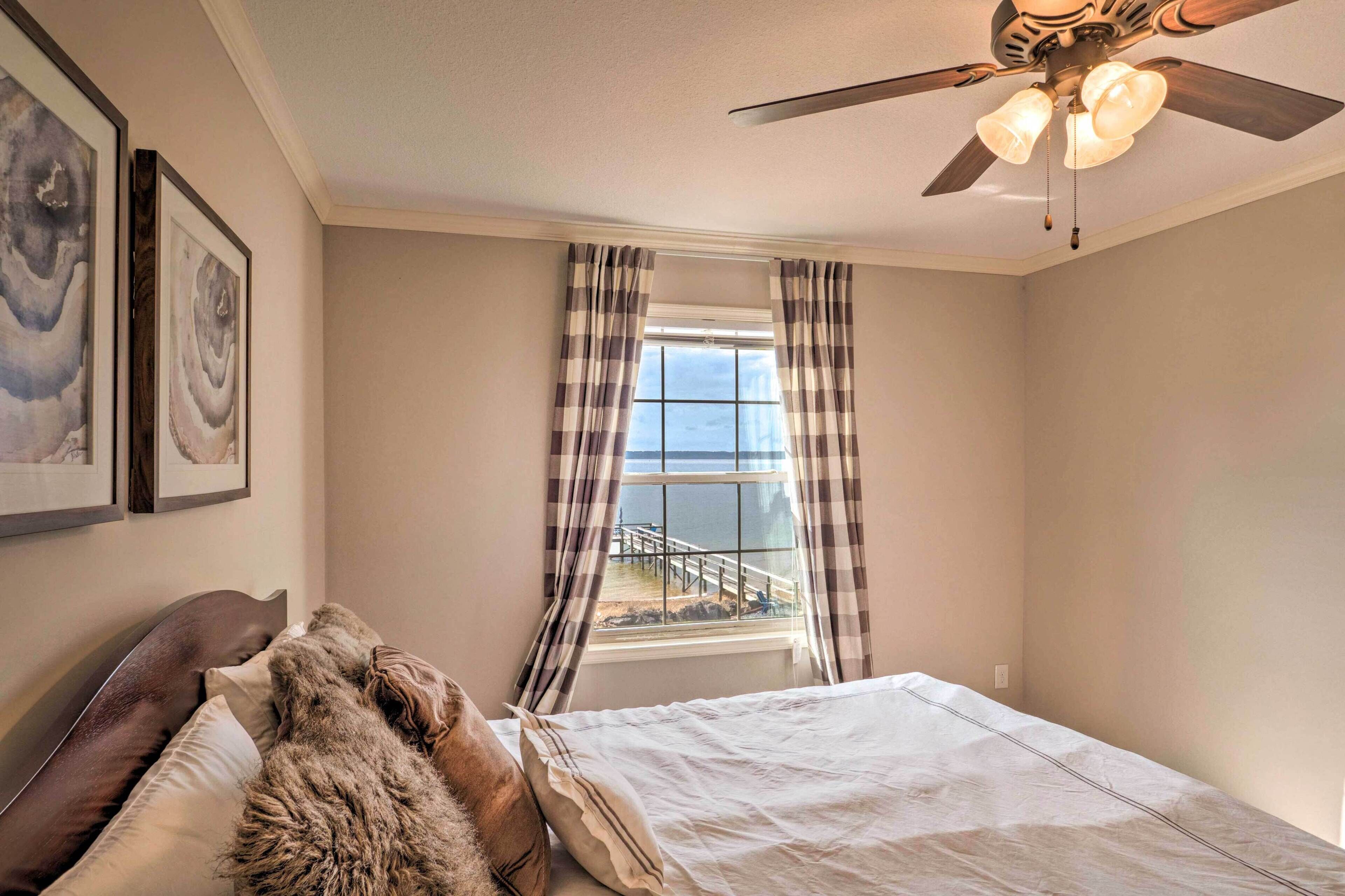 A bedroom with a bed, a ceiling fan, a window with curtains, and artwork on the wall.