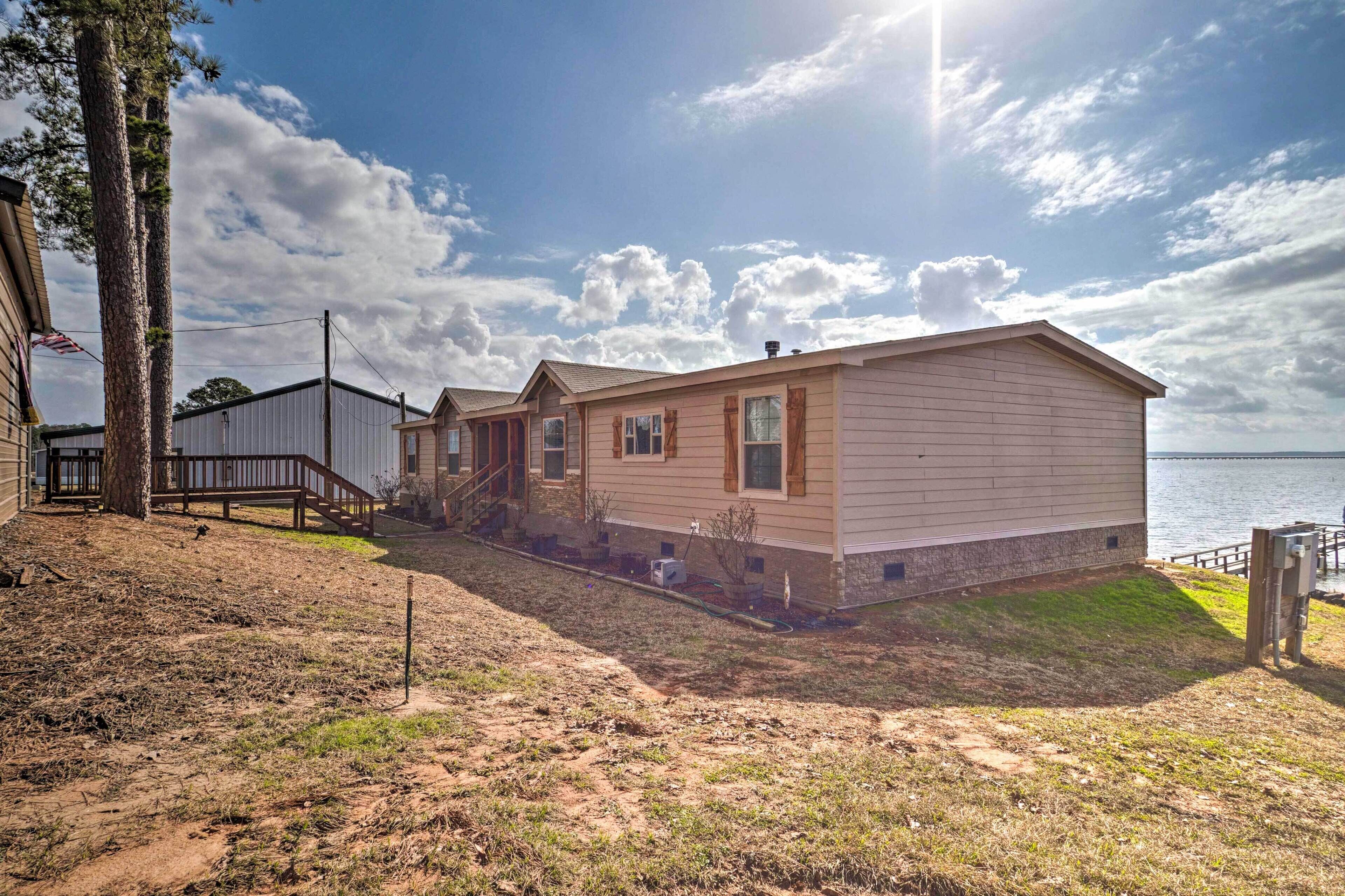 A single-story mobile home with a front porch, a small deck, and a view of the water.