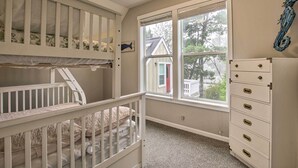 Una habitación con literas, un aparador y una ventana que da a una casa y árboles.