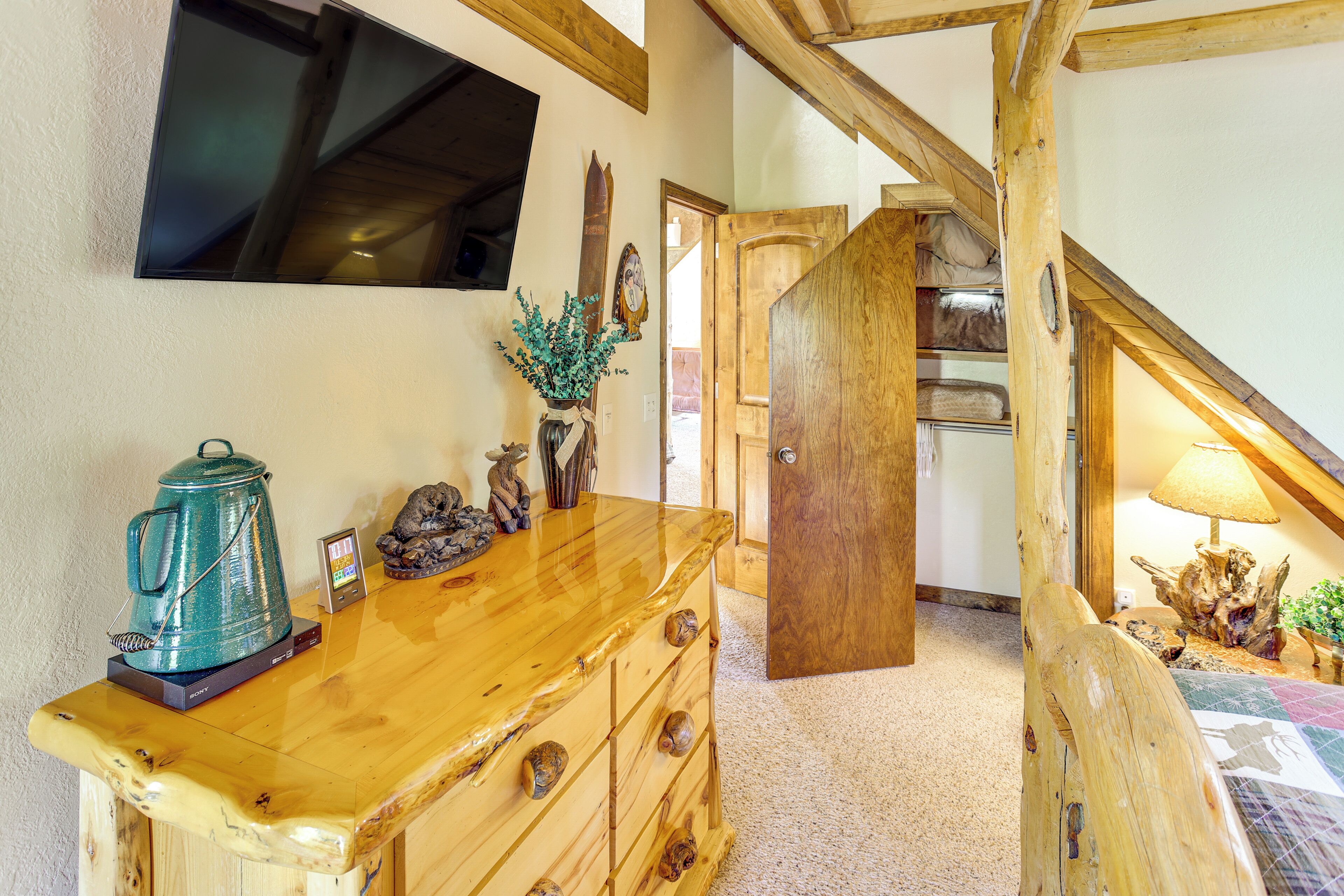 A wooden dresser with drawers, a kettle, and decorative items. A wooden staircase leads to a room with a lamp and a plant.