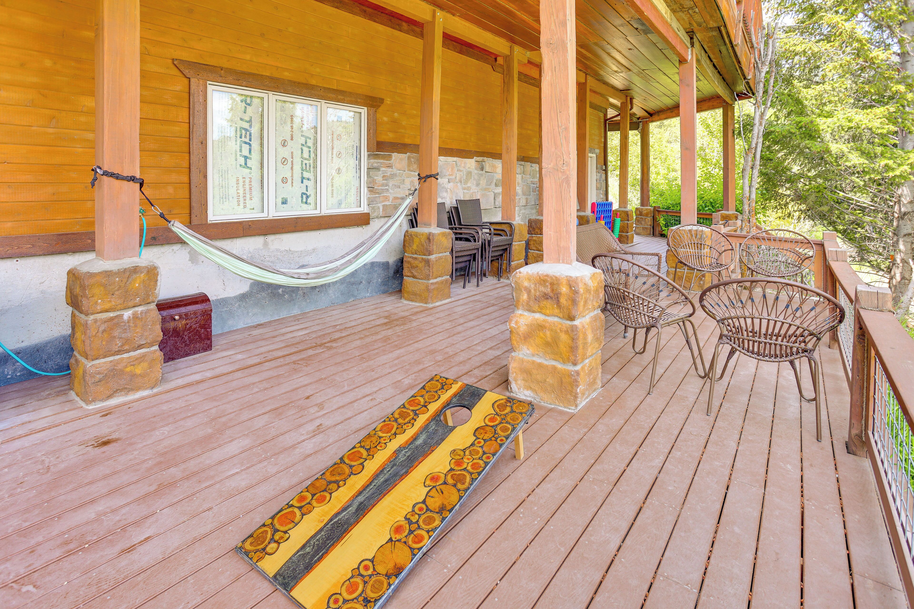 A wooden deck with a hammock, stone pillars, wicker chairs, and a table.