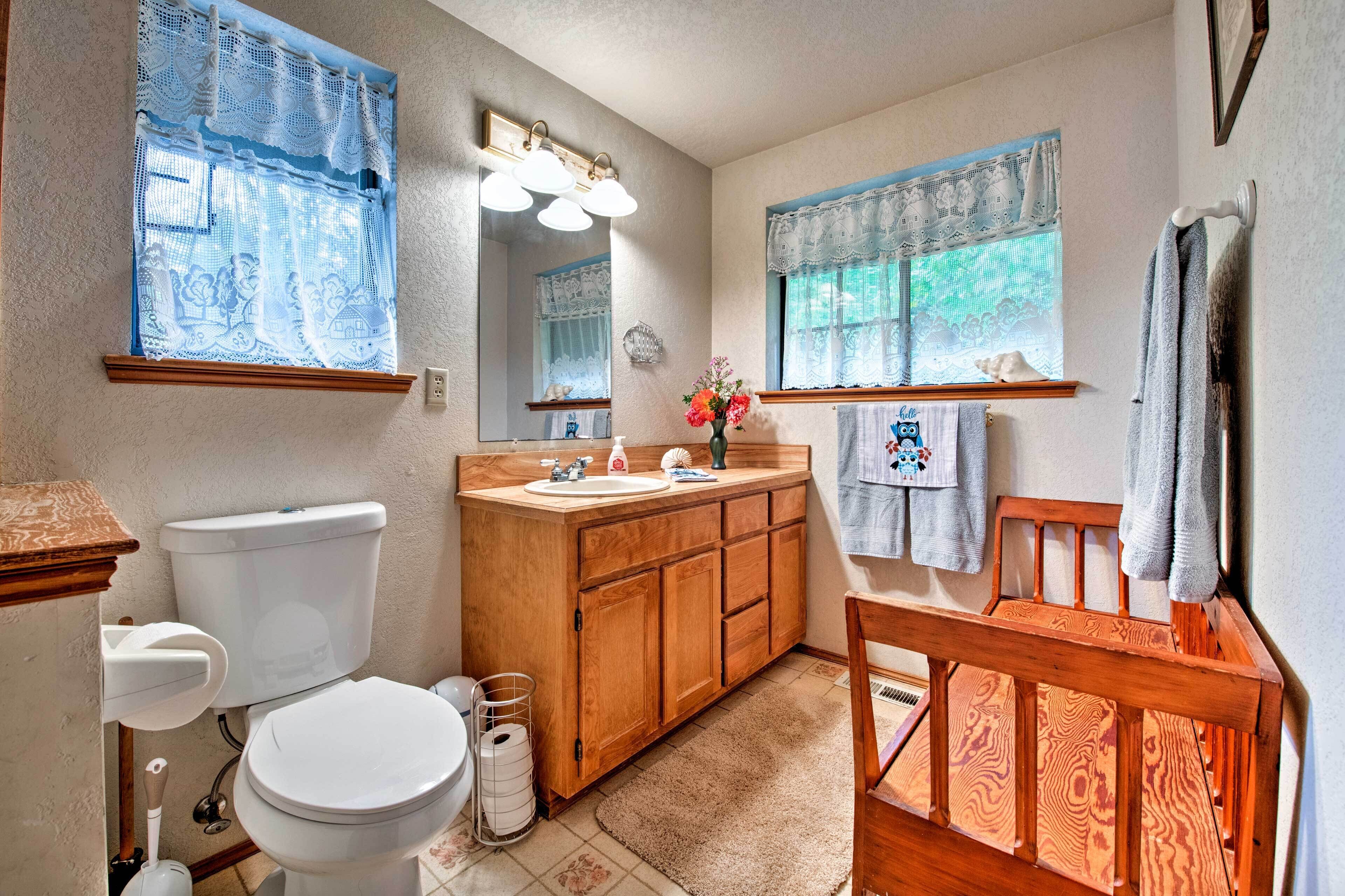 A bathroom with a toilet, sink, vanity, and wooden bench.