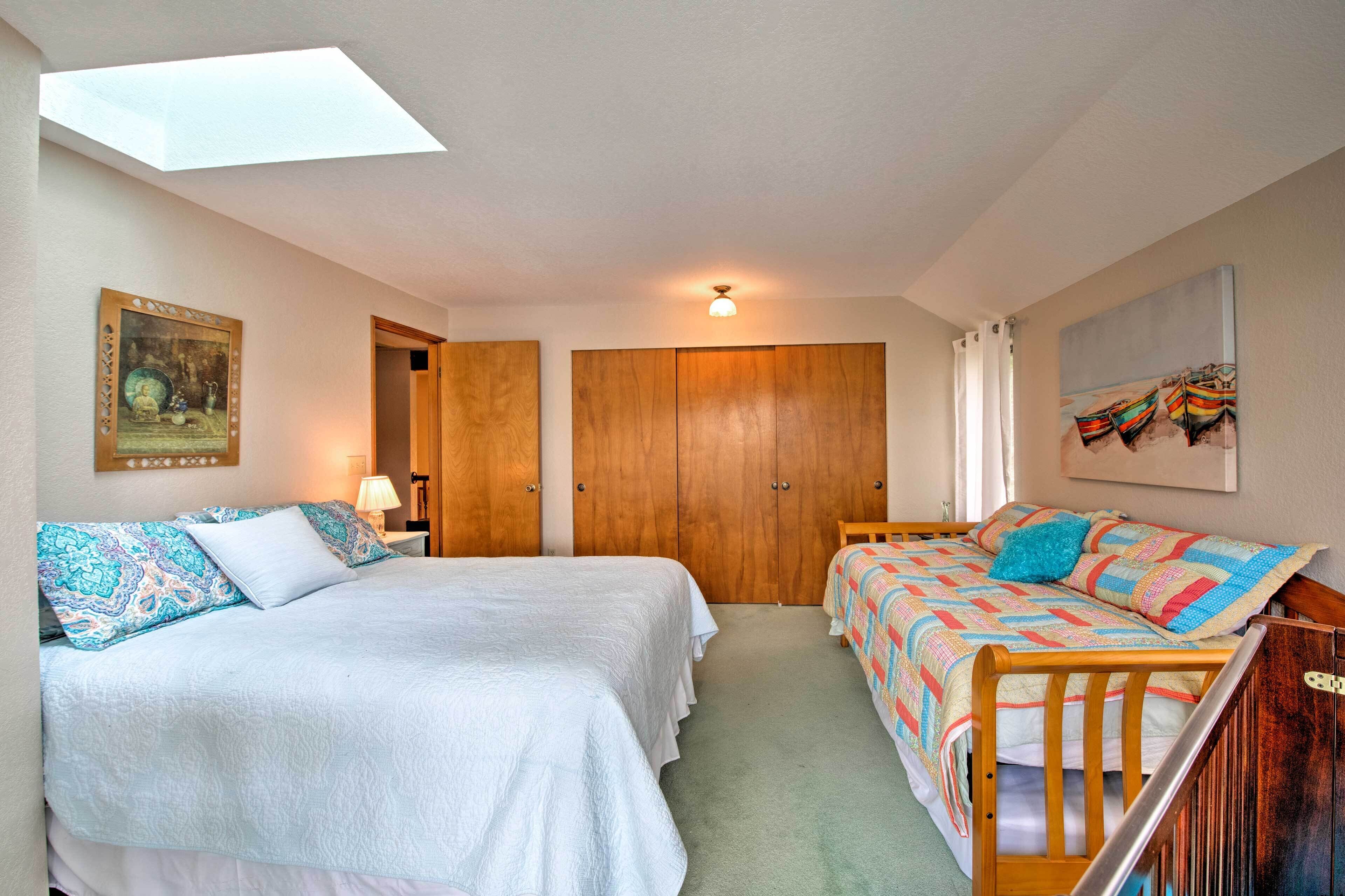 A bedroom with two beds, a skylight, a wooden wardrobe, a painting, and a window with curtains.