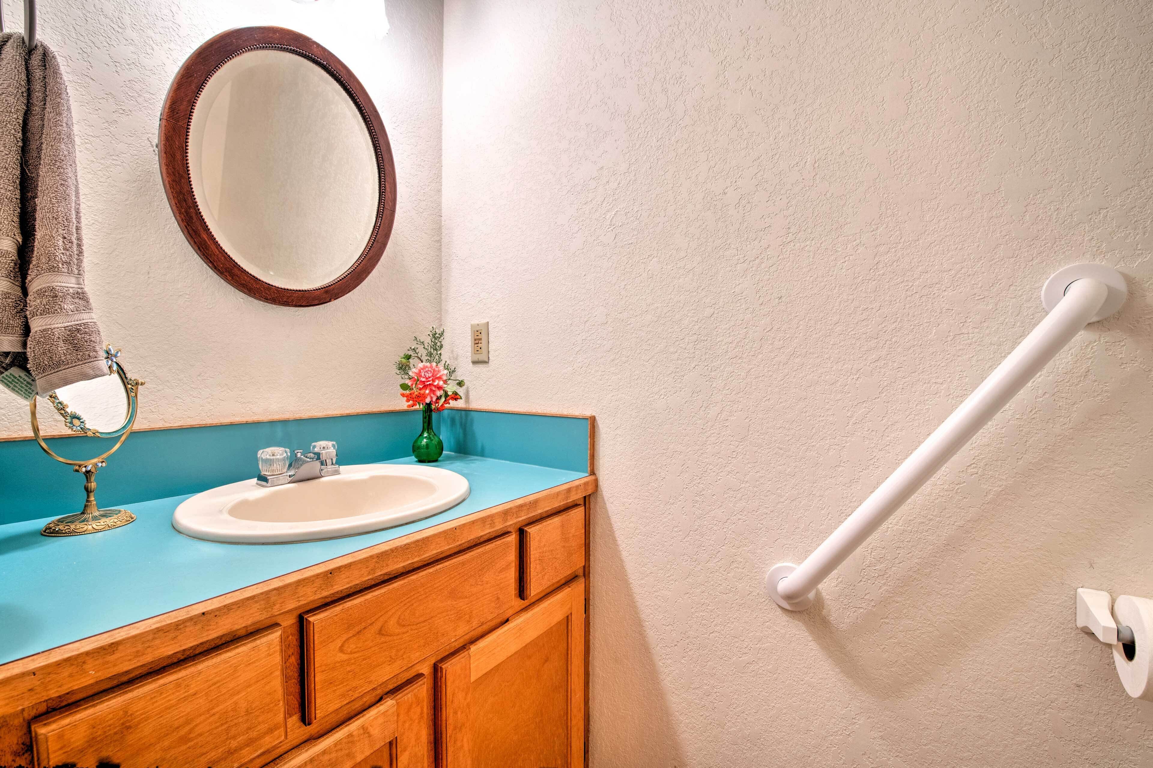 A bathroom with a wooden vanity, a white sink, a mirror, and a towel rack.