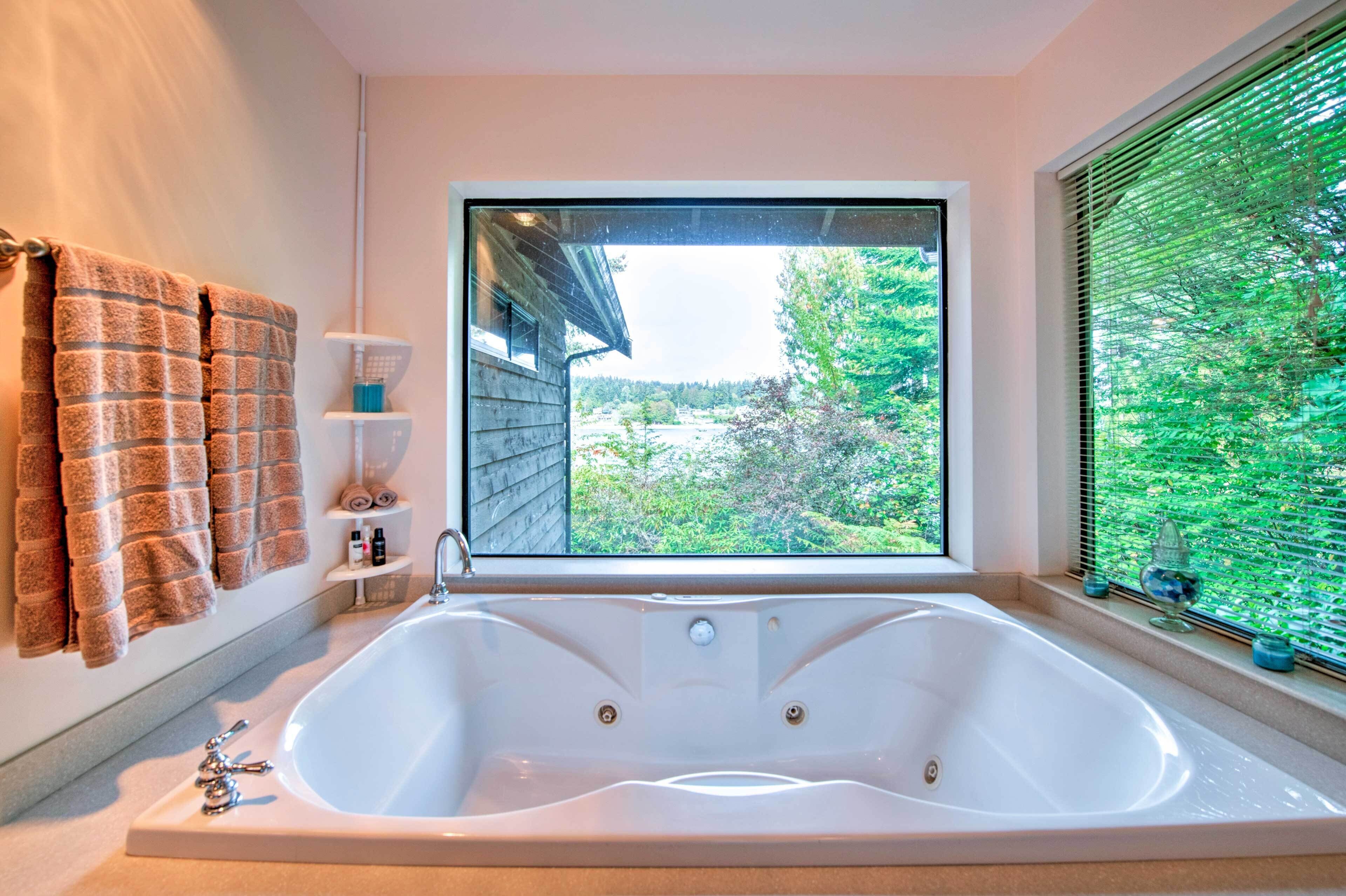 Un baño con una bañera grande, una ventana con vistas a la vegetación y toallas colgadas en la pared.