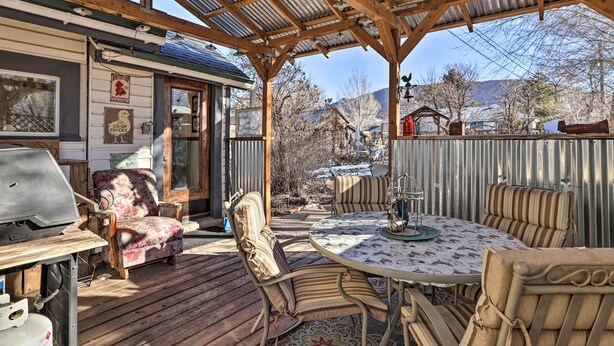 A covered patio with a wooden table and chairs, a grill, and a view of the surrounding area. - Charming Cedar City Retreat - Walk to Downtown! (Cedar City)