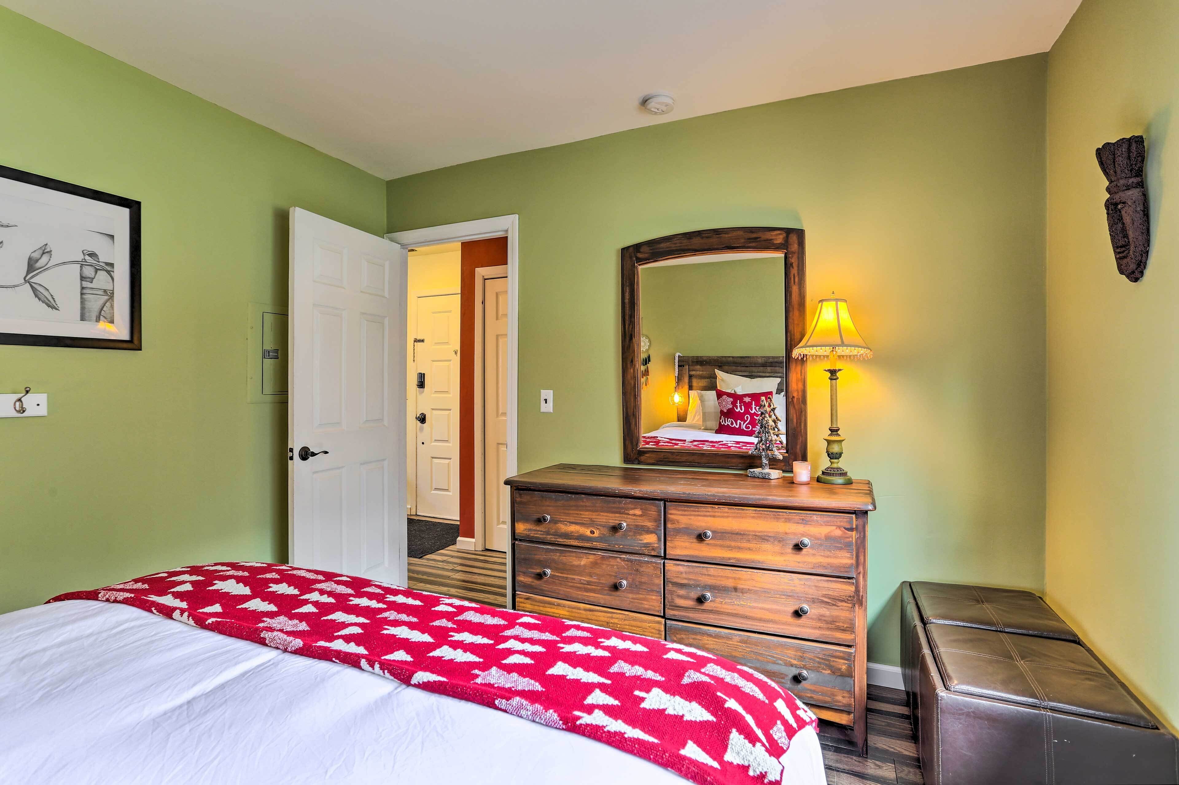 A bedroom with a bed, a dresser, a mirror, and a door.
