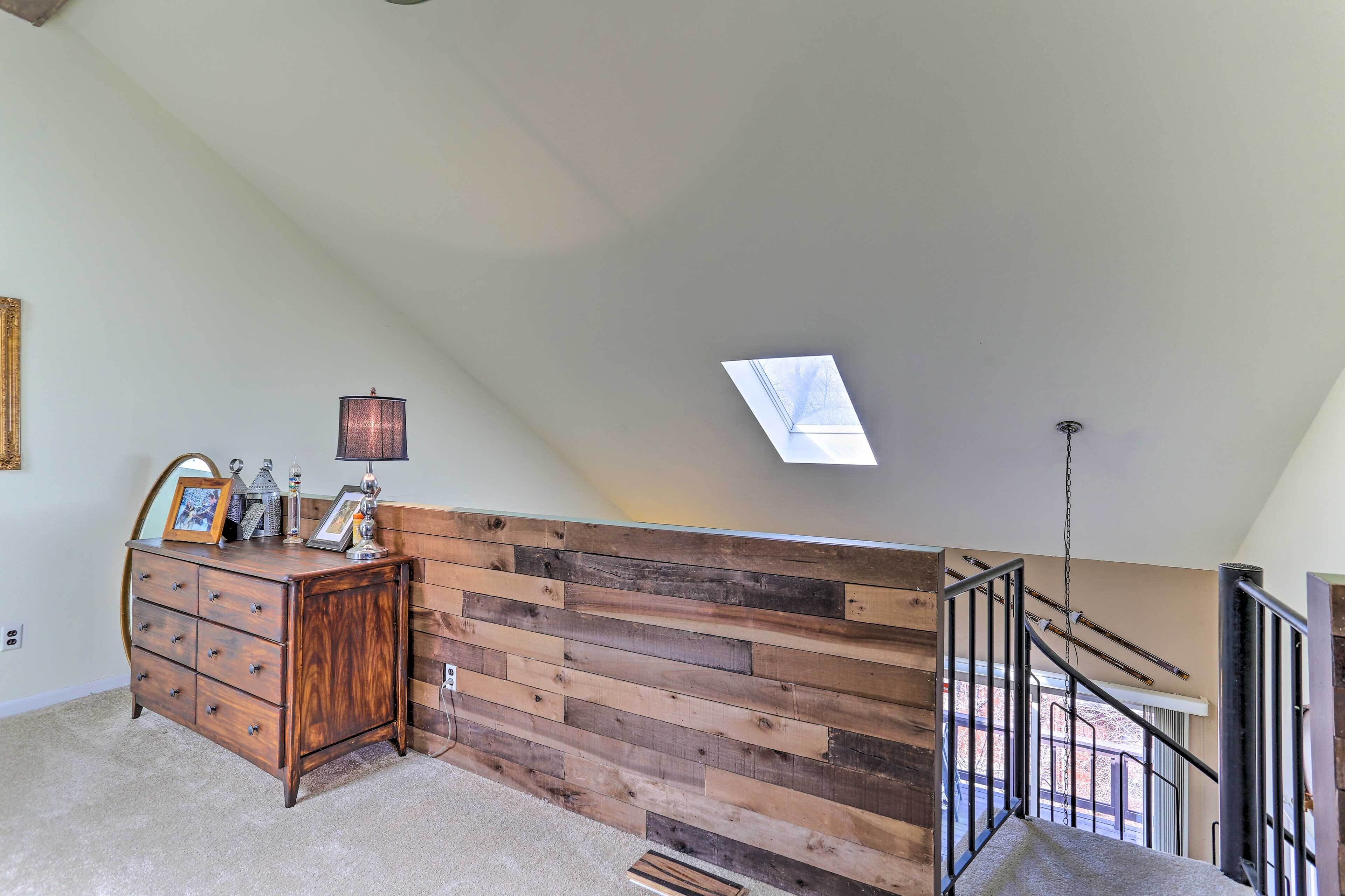 A room with a wooden wall, a dresser, a lamp, and a skylight.