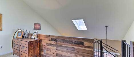 A room with a wooden wall, a dresser, a lamp, and a skylight.