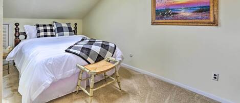 A bedroom with a bed, a chair, a painting, and a skylight.