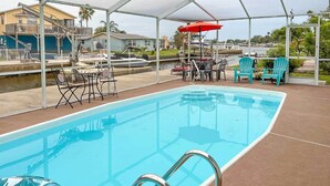 Une piscine avec un escalier en métal, entourée d’une zone abritée comprenant des chaises et des tables.