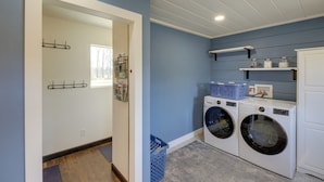 A laundry room with two front-loading washing machines, a blue laundry basket, and shelves with storage containers. - Pet-friendly Victor Home w/ Fire Pit & Large Yard! (Victor)