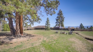 A backyard with a large tree, a wooden fence, and a small wooden structure. - Pet-friendly Victor Home w/ Fire Pit & Large Yard! (Victor)