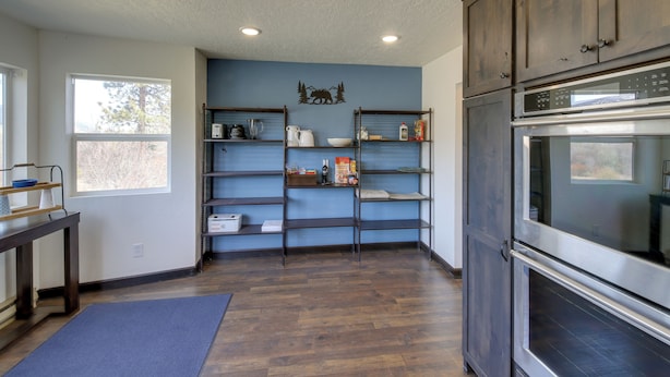 A kitchen with wooden cabinets, a stainless steel oven, and built-in shelves with kitchen items. - Pet-friendly Victor Home w/ Fire Pit & Large Yard! (Victor)