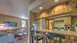 A kitchen with wooden cabinets, a bar area with stools, and a dining area with a sofa and coffee table. - Alto Adventure Base w/ Deck: Hike, Bike & Ski! (Alto)