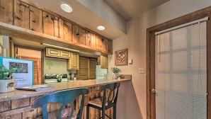 A kitchen with wooden accents, a bar area with two chairs, and a door with blinds. - Alto Adventure Base w/ Deck: Hike, Bike & Ski! (Alto)