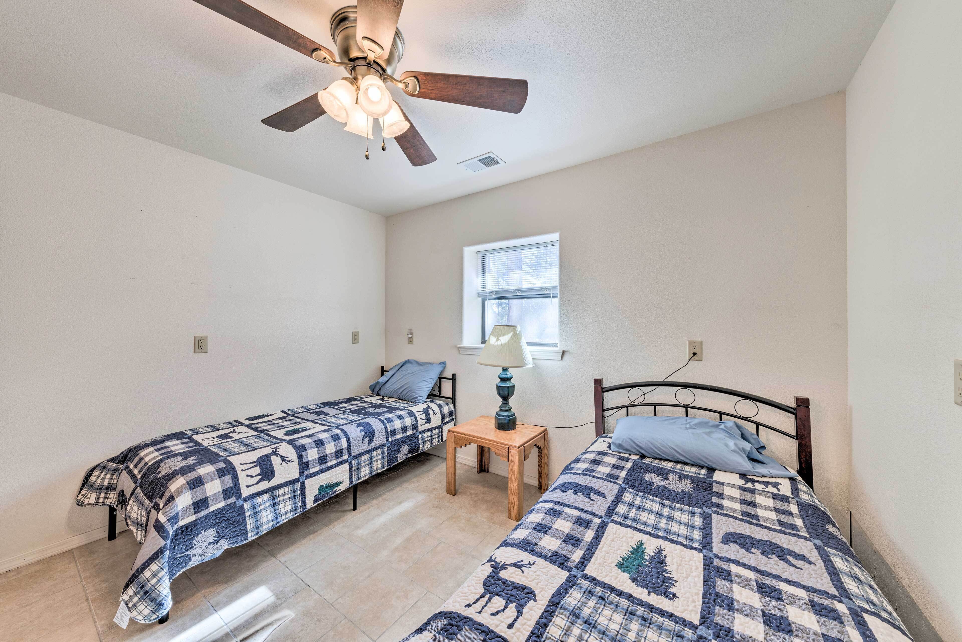 A bedroom with two single beds, a ceiling fan, a window, and a small table.