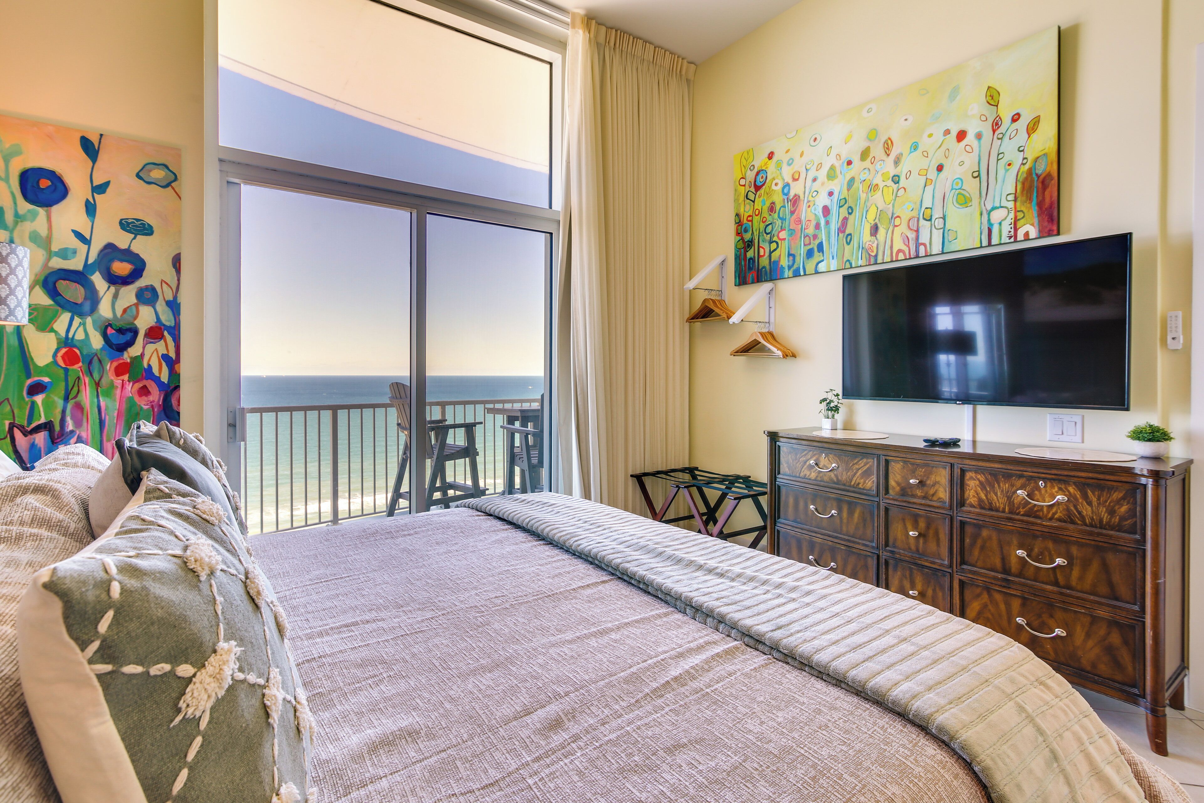 A bedroom with a large bed, a TV, a dresser, and a balcony with a view.