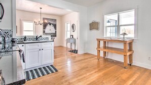 A modern kitchen with white cabinets, a black countertop, and a chandelier. There is a wooden table with a lamp on it. - Charming Choteau Cottage: Ski & Fish Nearby! (Choteau)