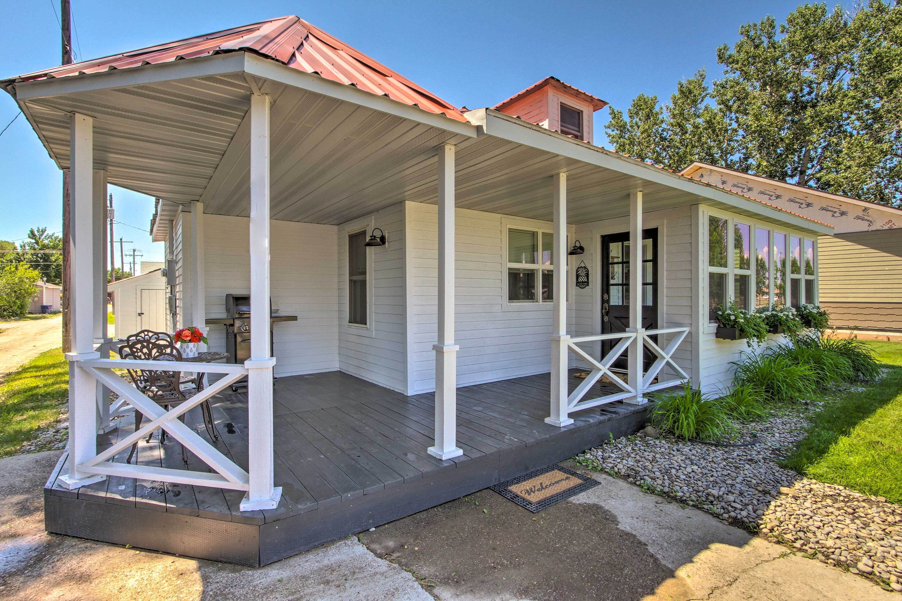 A covered porch with a wooden deck, white railings, and a small table with chairs.