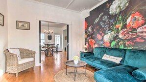 A living room with a wicker sofa, a teal velvet sofa, a round coffee table, and a floral painting on the wall. - Charming Choteau Cottage: Ski & Fish Nearby! (Choteau)